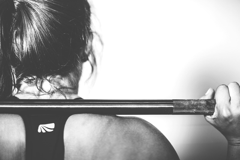 Woman holding a barbell across her back ready to squat as a muscle building exercise.